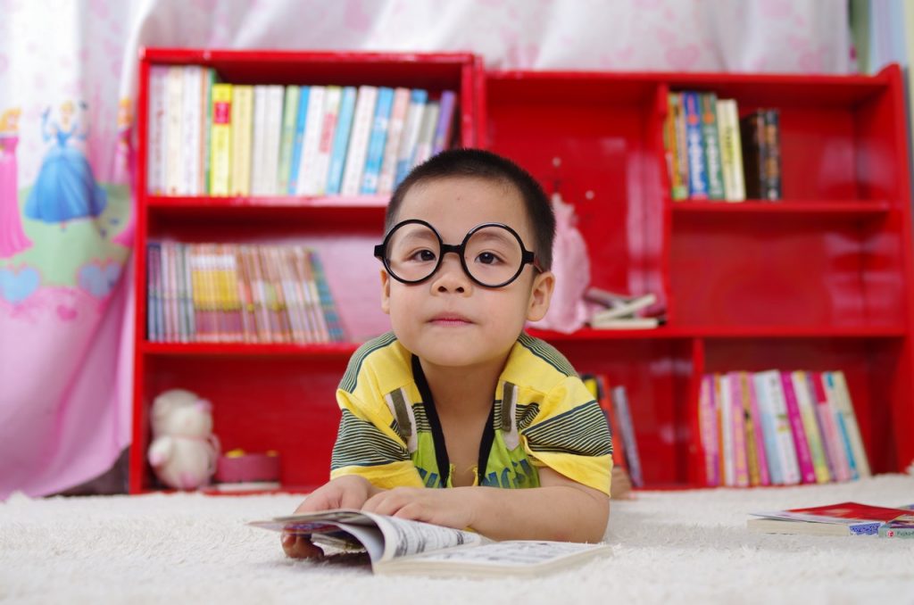 Ein kleiner Junge vor einem Bücherregal ließt ein Buch in seinem Kinderzimmer.