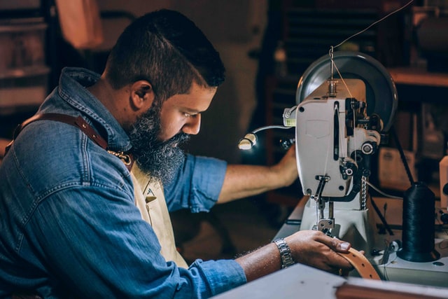 Ein mann sitzt an einer Nähmaschine und bearbeitet Kunstleder